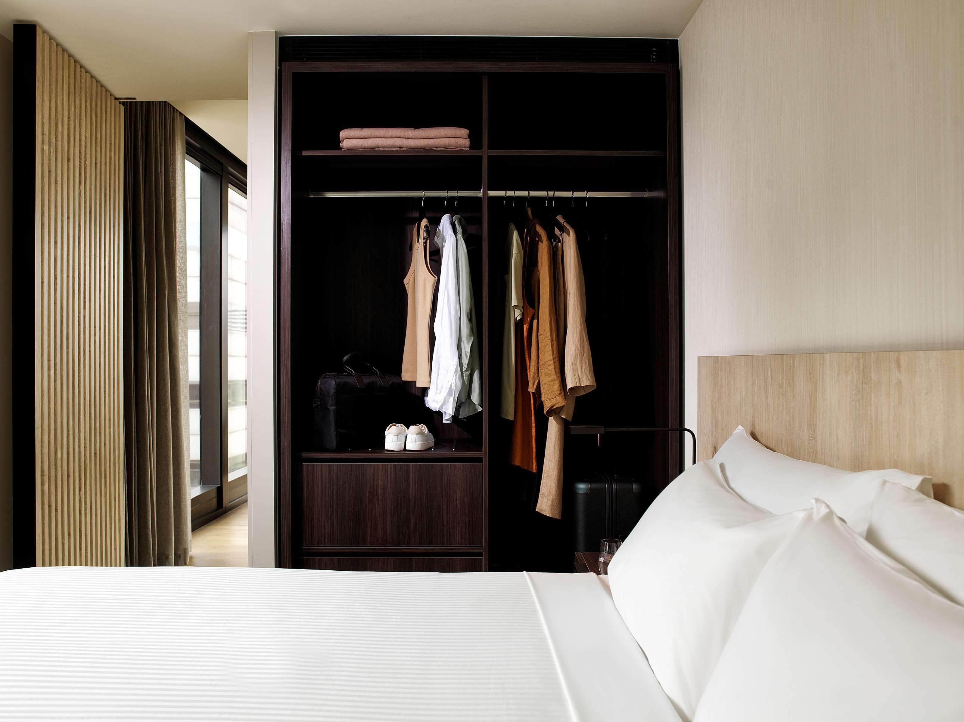 A hotel room with a large bed, a dark wooden wardrobe, and a window with curtains.