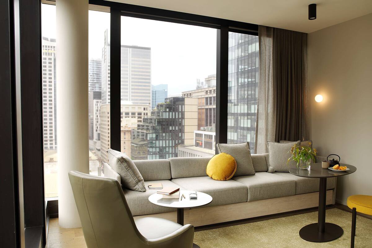 Un salon moderne avec un canapé, une table basse ronde et une vue sur le paysage urbain, visible à travers de grandes fenêtres.