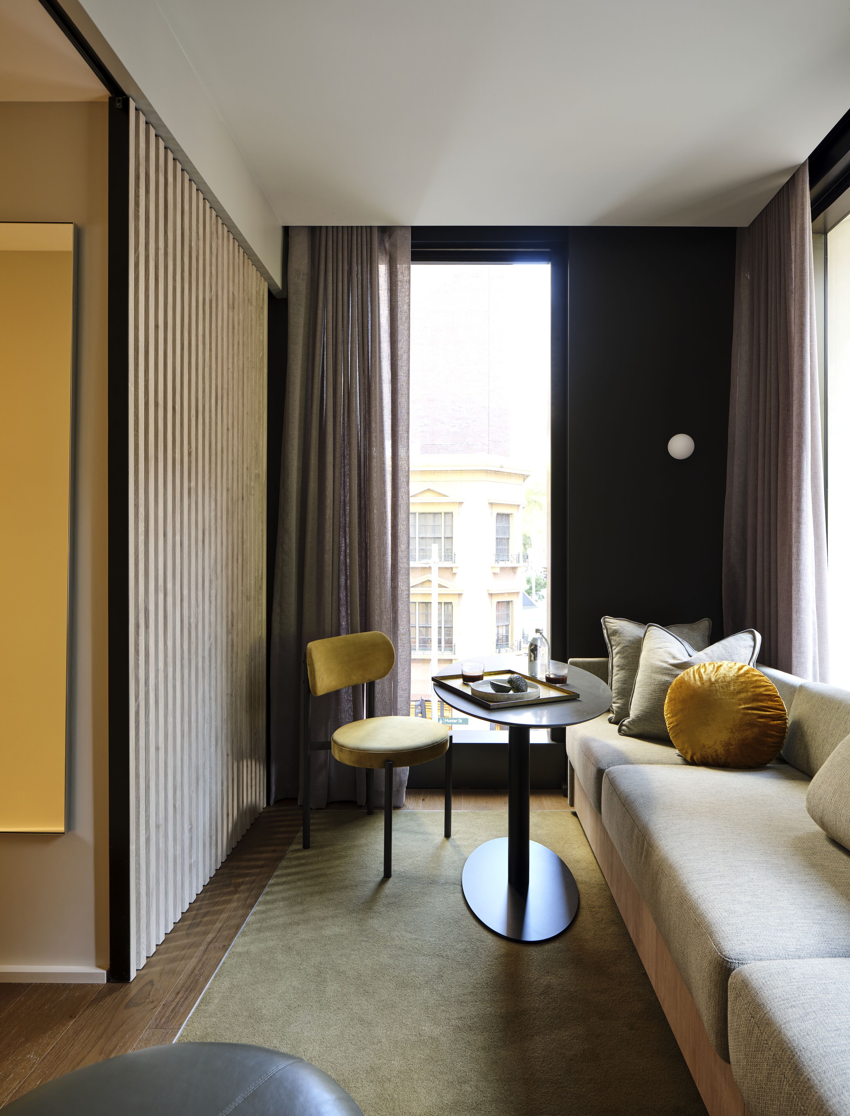 Una habitación de hotel moderna con un sofá, una silla, una mesita y vistas a un edificio.