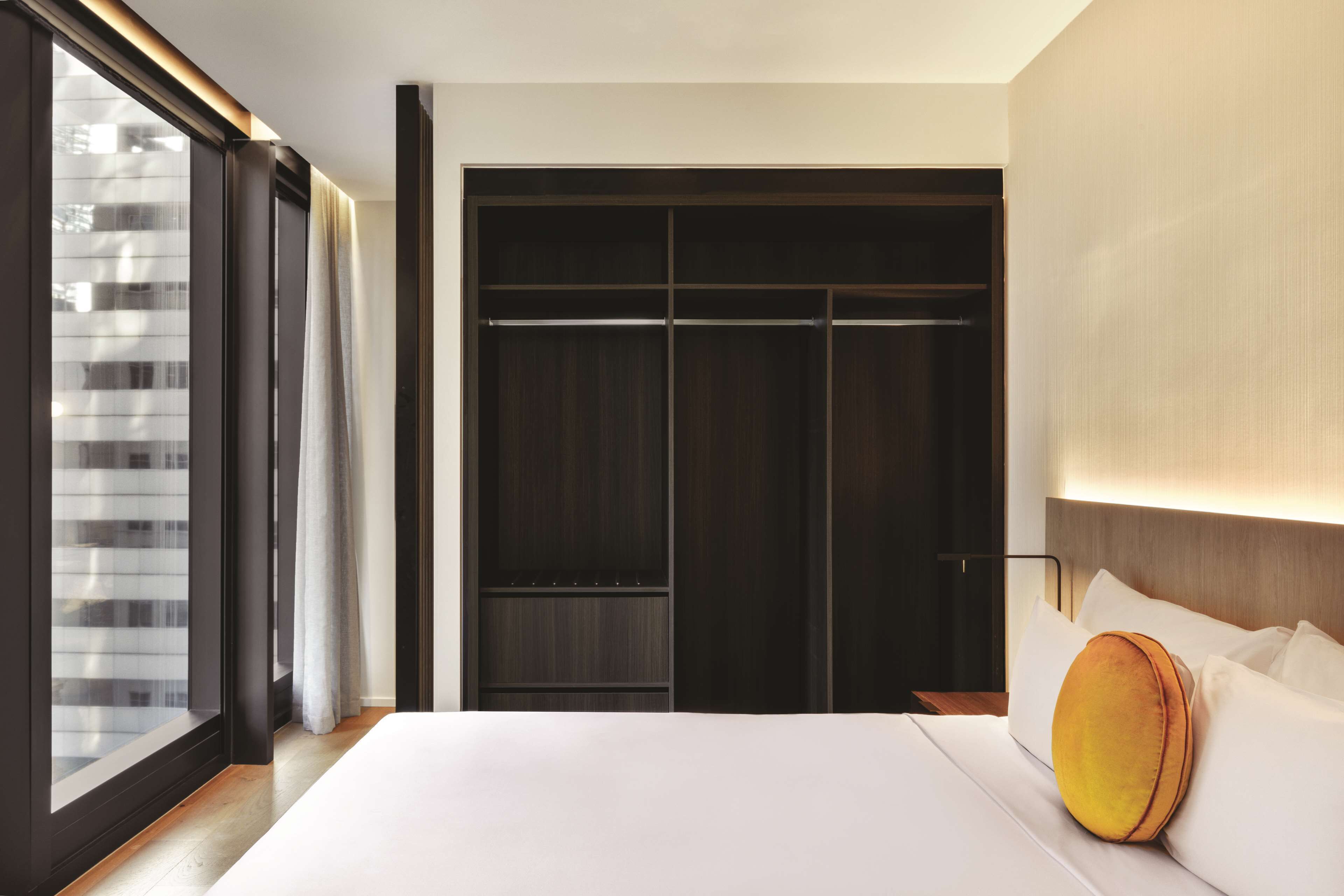 A hotel room with a large bed, a wardrobe, and a sliding glass door to the outside.