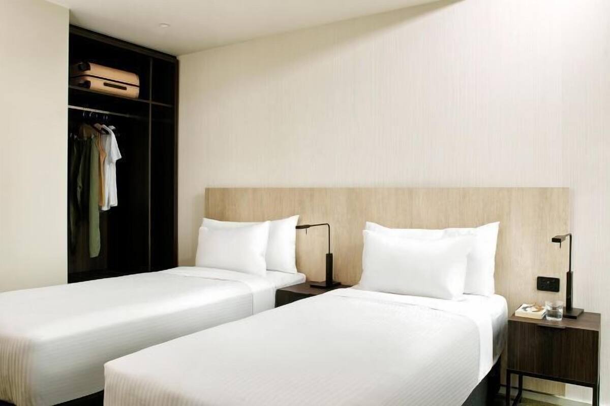 Une chambre d’hôtel avec deux lits simples, une armoire et une table de chevet avec une lampe.
