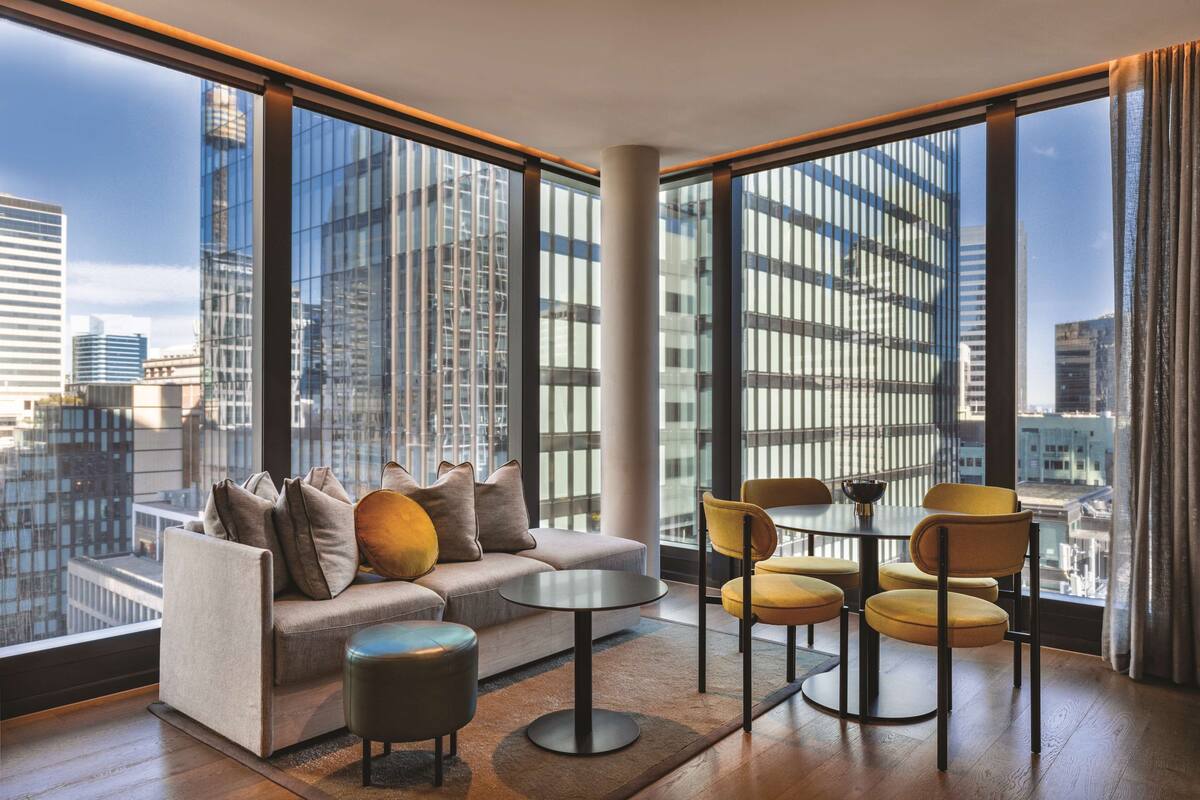 Un salon moderne avec un canapé, une table basse et des fauteuils, de grandes fenêtres offrant une vue sur la ville et un plancher en bois.