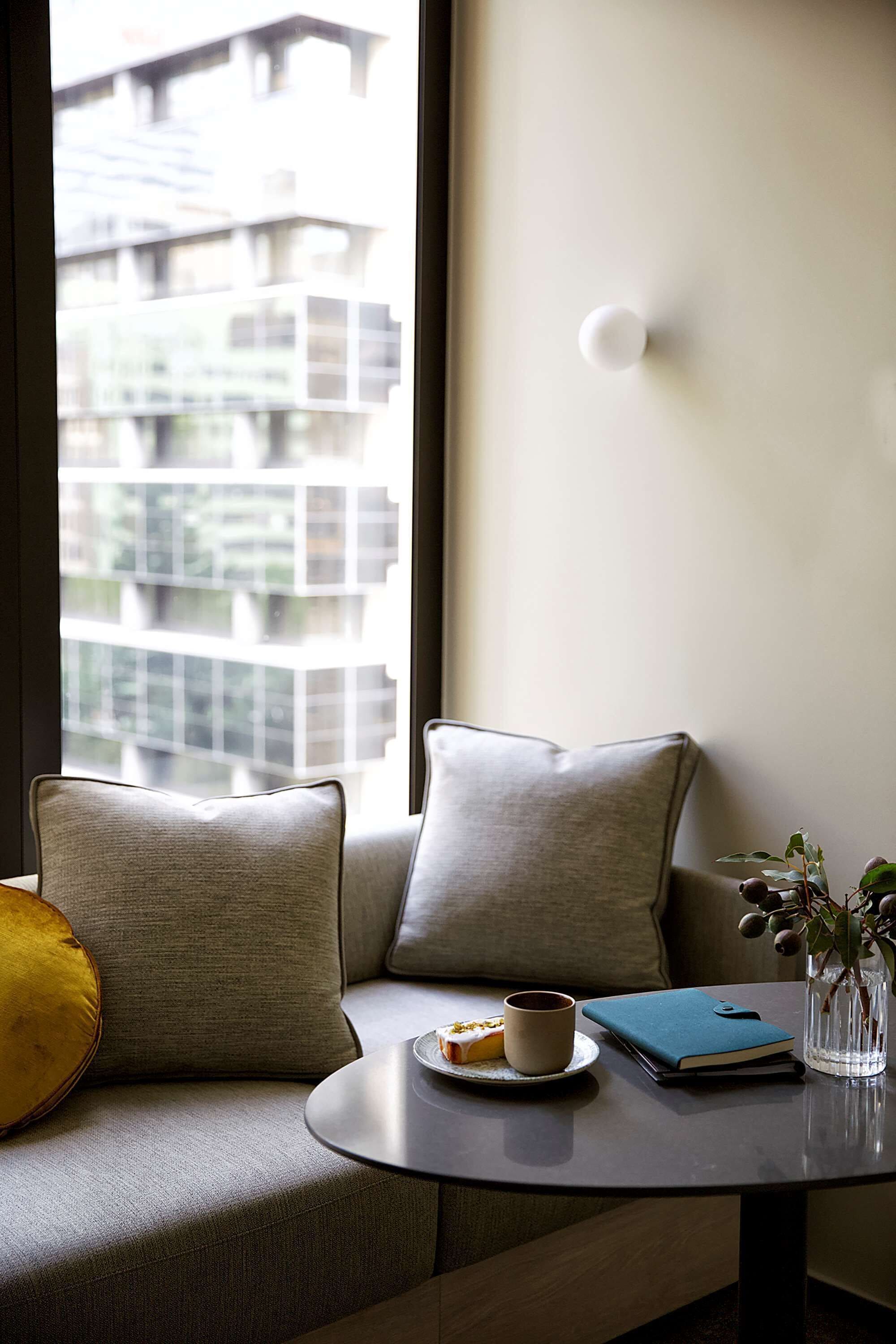 A modern living room with a sofa, a small round table, a cup, a book, and a vase with a plant.