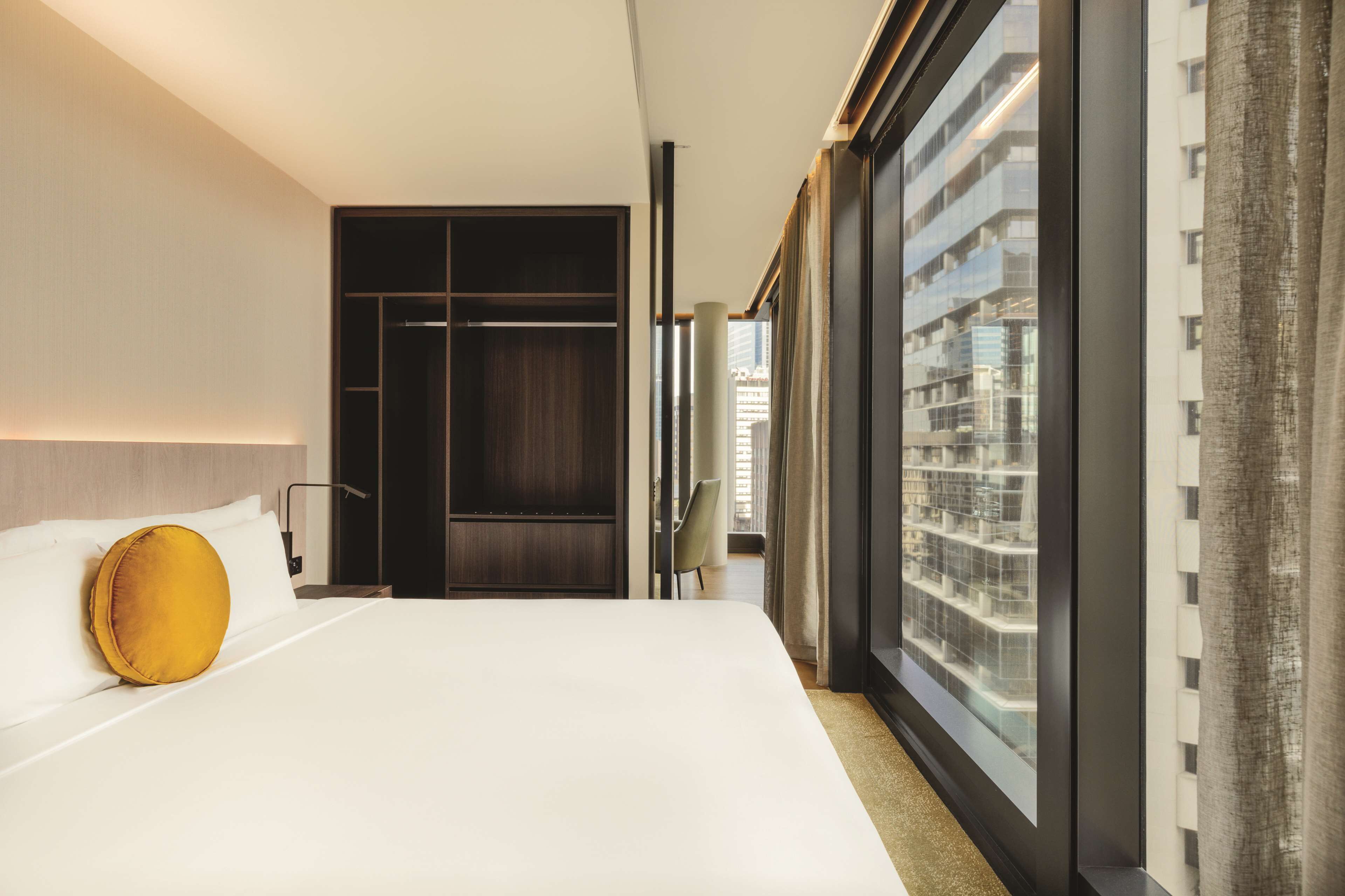 A hotel room with a large bed, a wardrobe, and a window with a city view.