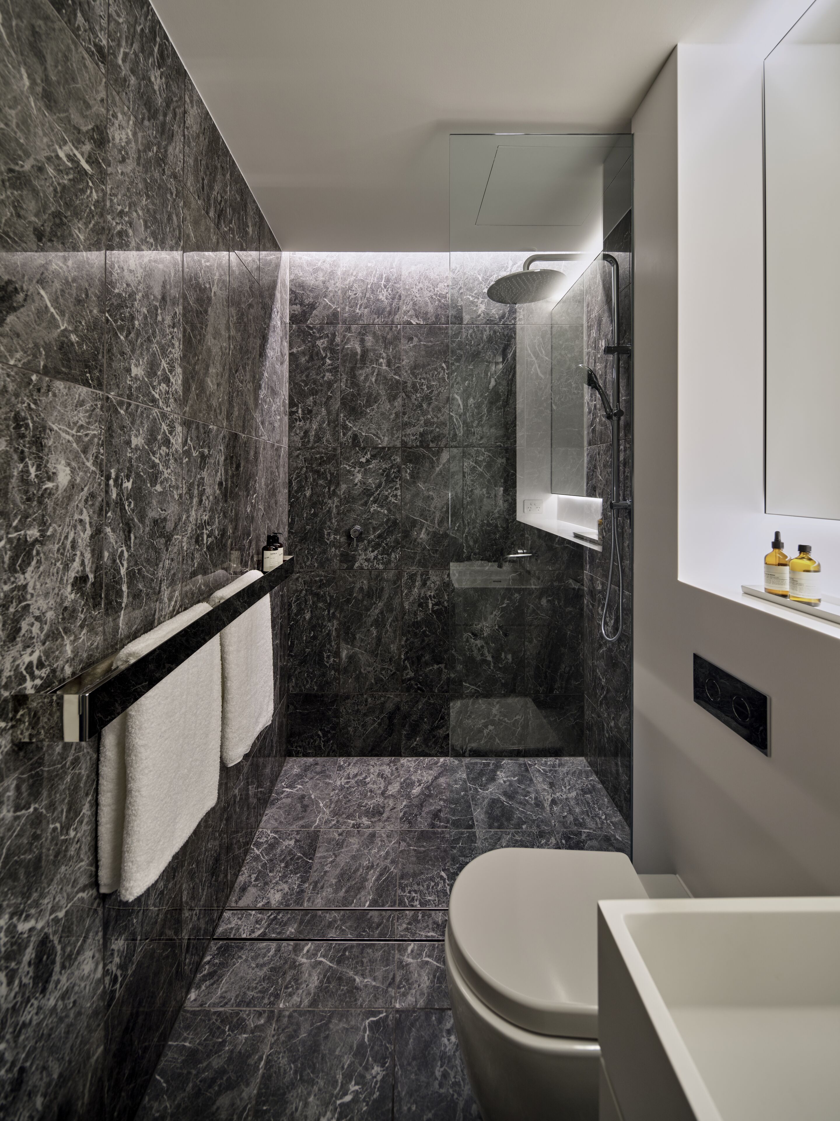 Un baño moderno con ducha de mármol, inodoro y lavamanos.