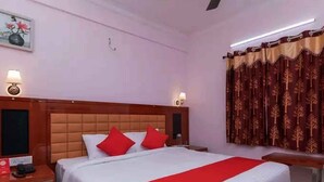 A hotel room with a large bed, red pillows, a wooden headboard, bedside lamps, a nightstand, a telephone, and a window with patterned curtains. - Swarnam Residency (Chennai)