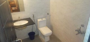 A small bathroom with a white toilet, a sink with a mirror above it, and a showerhead on the wall. - Swarnam Residency (Chennai)