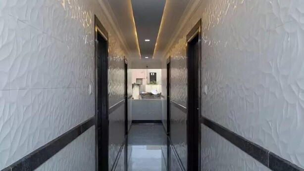 A corridor with textured walls and a reflective floor, leading to a room with a kitchen area visible in the background. - Swarnam Residency (Chennai)