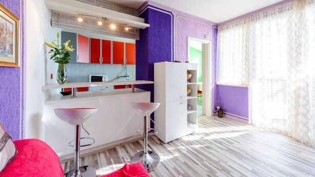 Una cocina moderna con armarios rojos y blancos, una encimera blanca y una pared de acento morada.