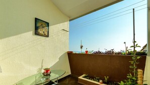 Un balcón con una mesa de vidrio, plantas en macetas y un cuadro en la pared.