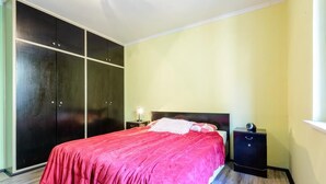 Un dormitorio con cama, mesita de noche, armario y ventana.