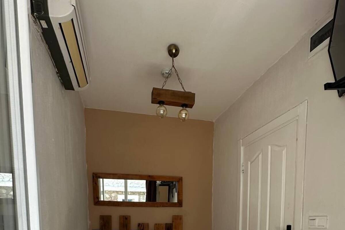 Un dormitorio con estructura de cama de madera, ventilador de techo, espejo sobre la cama y una puerta a la derecha.