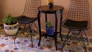 Une pièce comprenant deux chaises au design épuré, en fil de métal noir, une petite table ronde ornée d’un pot de plante et un tableau représentant une feuille aux couleurs vives accroché au mur.