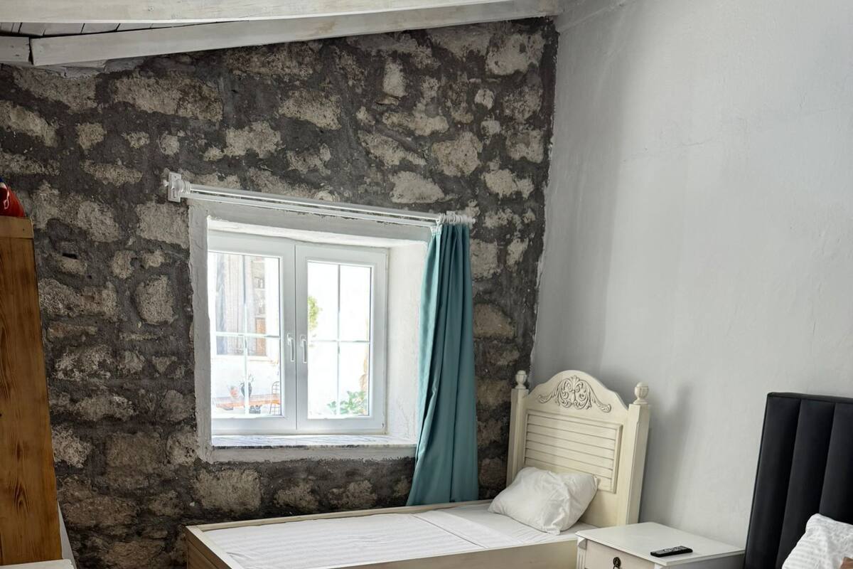 Una habitación con dos camas, una ventana con cortinas, piso de madera y pared de piedra.