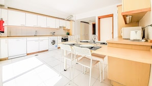 A modern kitchen with white cabinets, a washing machine, and a dining area with white chairs and a table set for four.