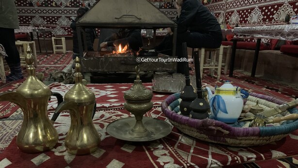 A traditional setting with a central fire, brass water containers, a teapot, and a woven tray with utensils. - Get Your Night in Wadi Rum (Wadi Rum)