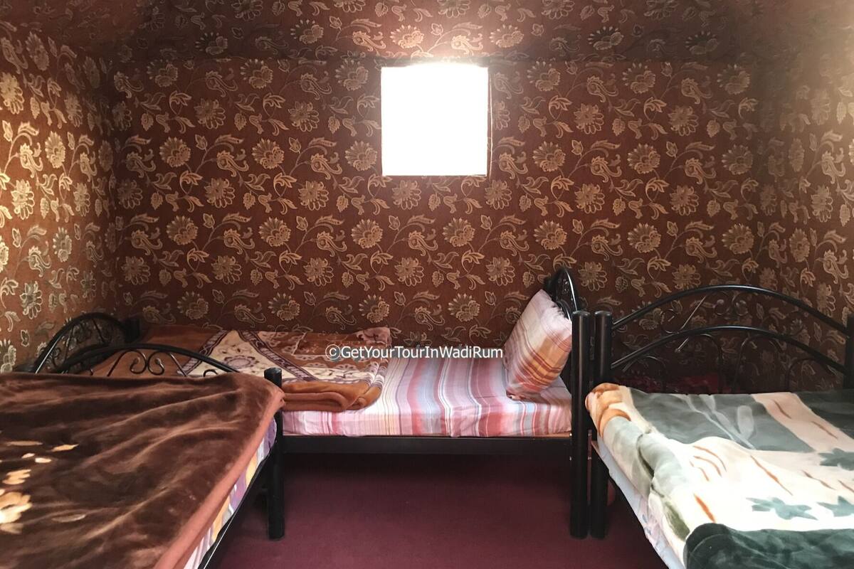 Une petite pièce agréable, avec un papier peint à motifs floraux, une seule fenêtre et deux lits.