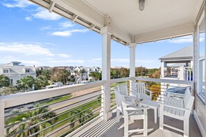 Un balcón con sillas y mesa blancos, con vistas a una calle con palmeras y casas.