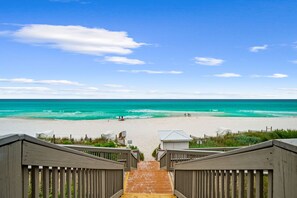 A wooden staircase leading to a beach with clear turquoise water and a clear sky.