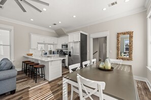 Una cocina moderna con armarios blancos, una isla central con taburetes y un comedor con mesa y sillas.