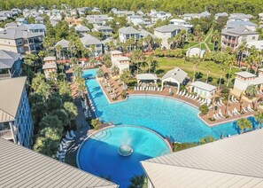 A resort with a large swimming pool surrounded by lounge areas and palm trees.