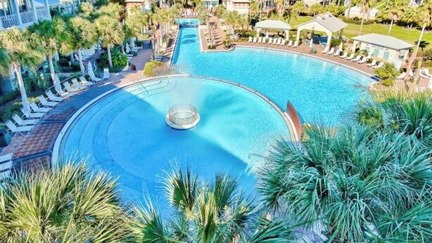Ein großer Pool, umgeben von Palmen und Liegestühlen, mit einer runden Wasserspielsituation in der Mitte.