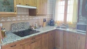 A kitchen with wooden cabinets, a granite countertop, a built-in oven, and a window with curtains. - Rural house Majaceite (El Bosque)