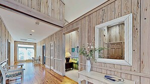 A spacious hallway with wooden paneling, a white console table with a vase, and a bench with patterned cushions. - Marlin Spectacular Ocean View, Inlet Point South, Beach, Pool (Pawleys Island)