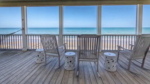 A covered deck with wooden flooring, three wooden chairs, and two decorative stools. - Marlin Spectacular Ocean View, Inlet Point South, Beach, Pool (Pawleys Island)