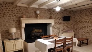 A dining area with a fireplace, a table set for four, and a television mounted on the wall. - 1 bedroom Country Cottage (Suaux)