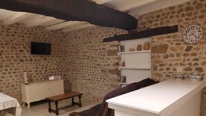 A rustic kitchen with stone walls, a wooden bench, a white counter, and a clock on the wall. - 1 bedroom Country Cottage (Suaux)