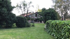A well-maintained grassy area with a stone building in the background, surrounded by dense foliage. - 1 bedroom Country Cottage (Suaux)