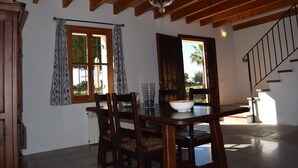 A dining area with a wooden table and chairs, a chandelier, and a view of the outdoors through a window. - Punta de Vistalegre is a Villa with a Private Pool in a Very Quiet Rural Setting (Porto Cristo)
