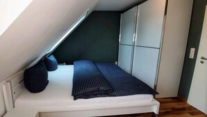 A small, compact bedroom with a bed, dark pillows, and a wardrobe. - DHH "lütte Sprotte" (St. Peter-Ording)