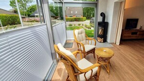 A modern living room with wicker furniture, a glass door leading outside, a fireplace, and a television. - DHH "lütte Sprotte" (St. Peter-Ording)
