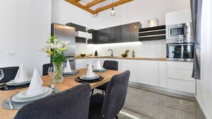 Een moderne keuken met witte kastjes, een houten plafond en een eethoek met een tafel, stoelen en een bloevas.