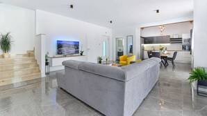Een moderne woonkamer met een grijze modulaire bank, een flatscreen televisie en een eethoek met een gele stoel.