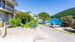 A coastal street with a parked car, a stone wall, and a building with balconies.