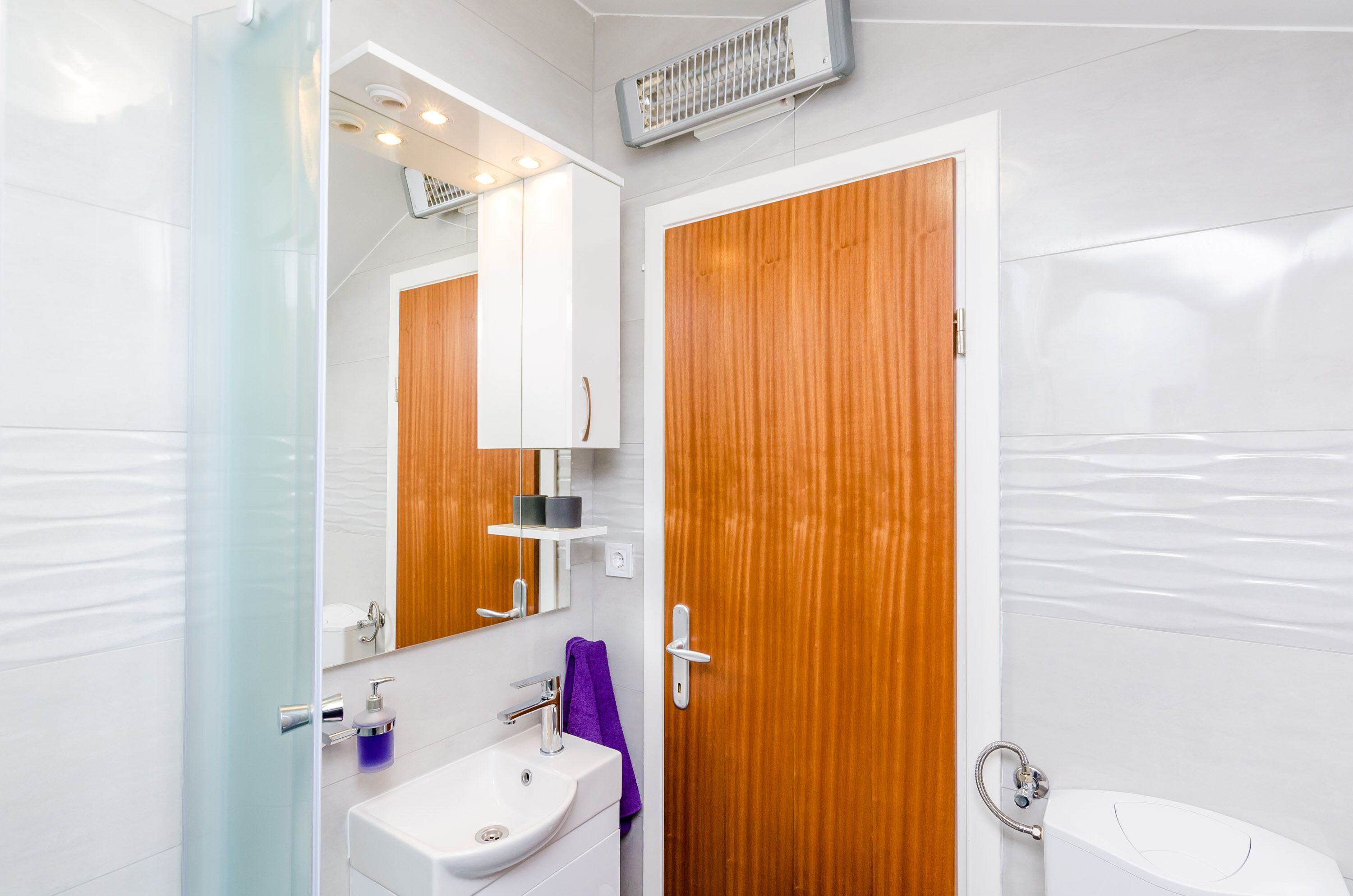 Un baño con cabina de ducha de vidrio, un lavamanos blanco y una toalla morada, además de una puerta de madera.