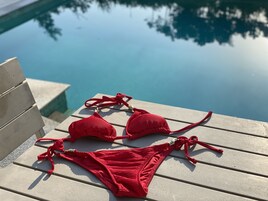 Un bikini rojo sobre una cubierta de madera junto a una piscina.