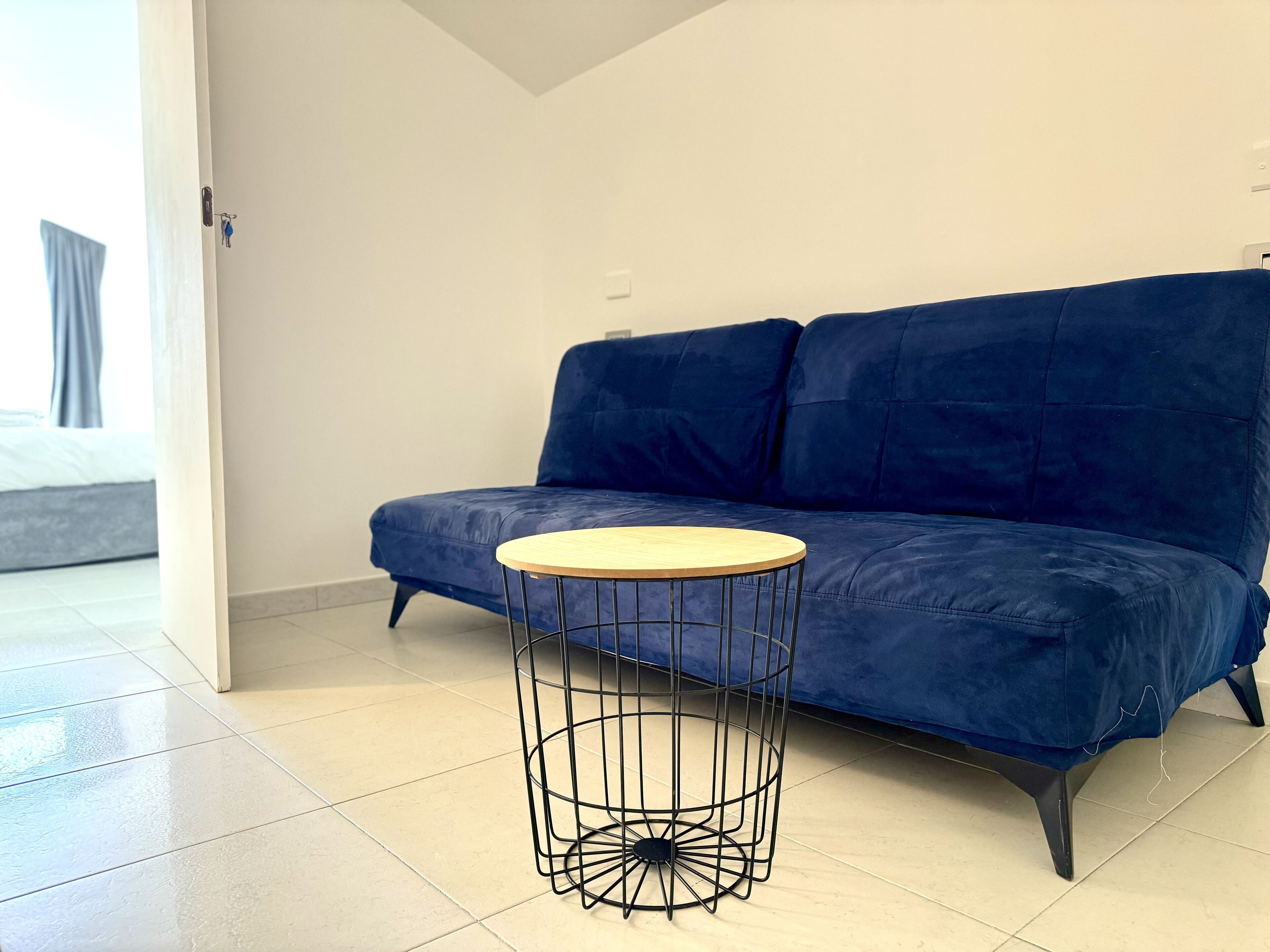 A modern living room with a blue sofa and a round wooden coffee table with a wireframe base.