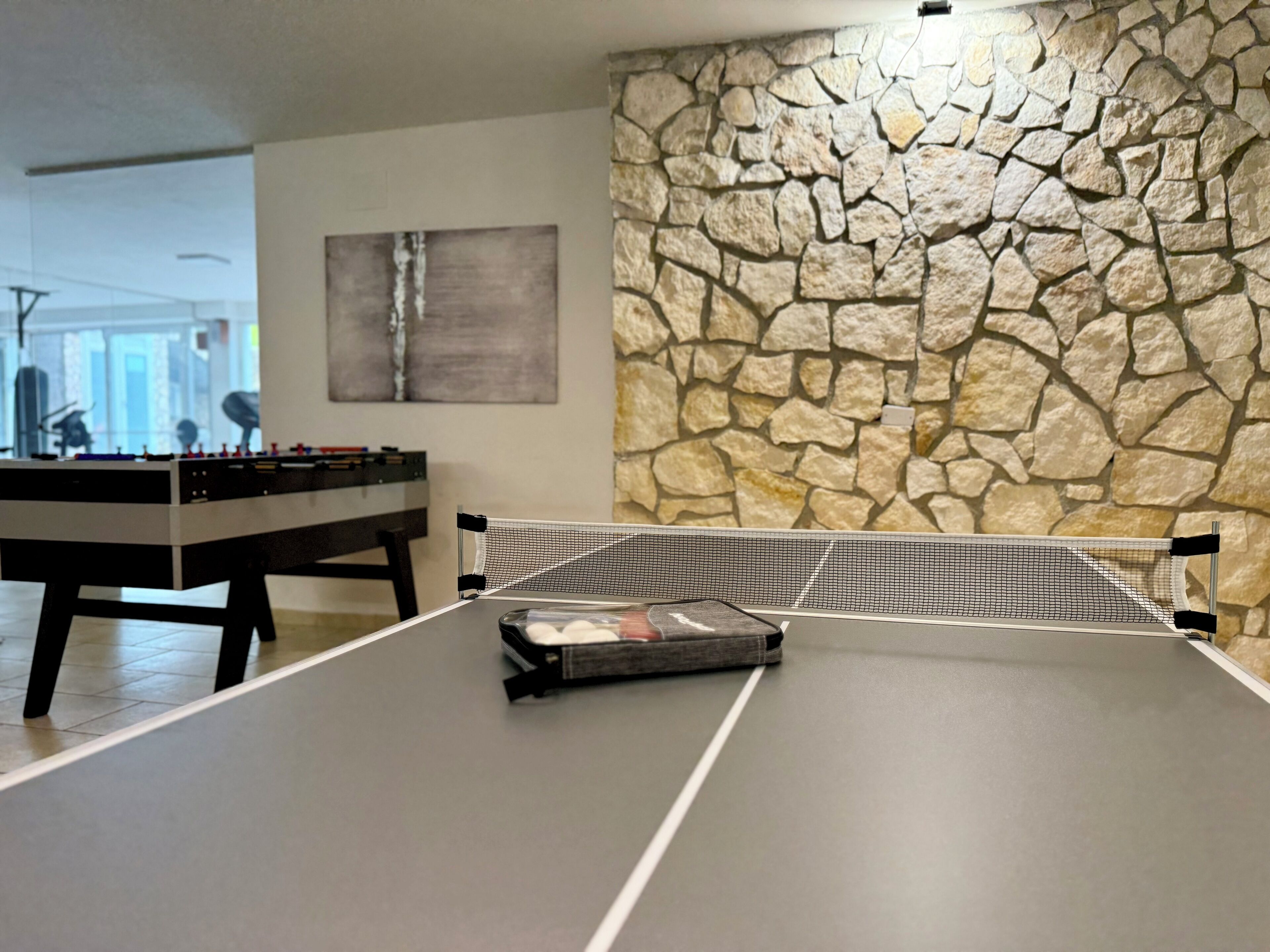 A ping pong table with a net in a room with a stone wall and a foosball table in the background.