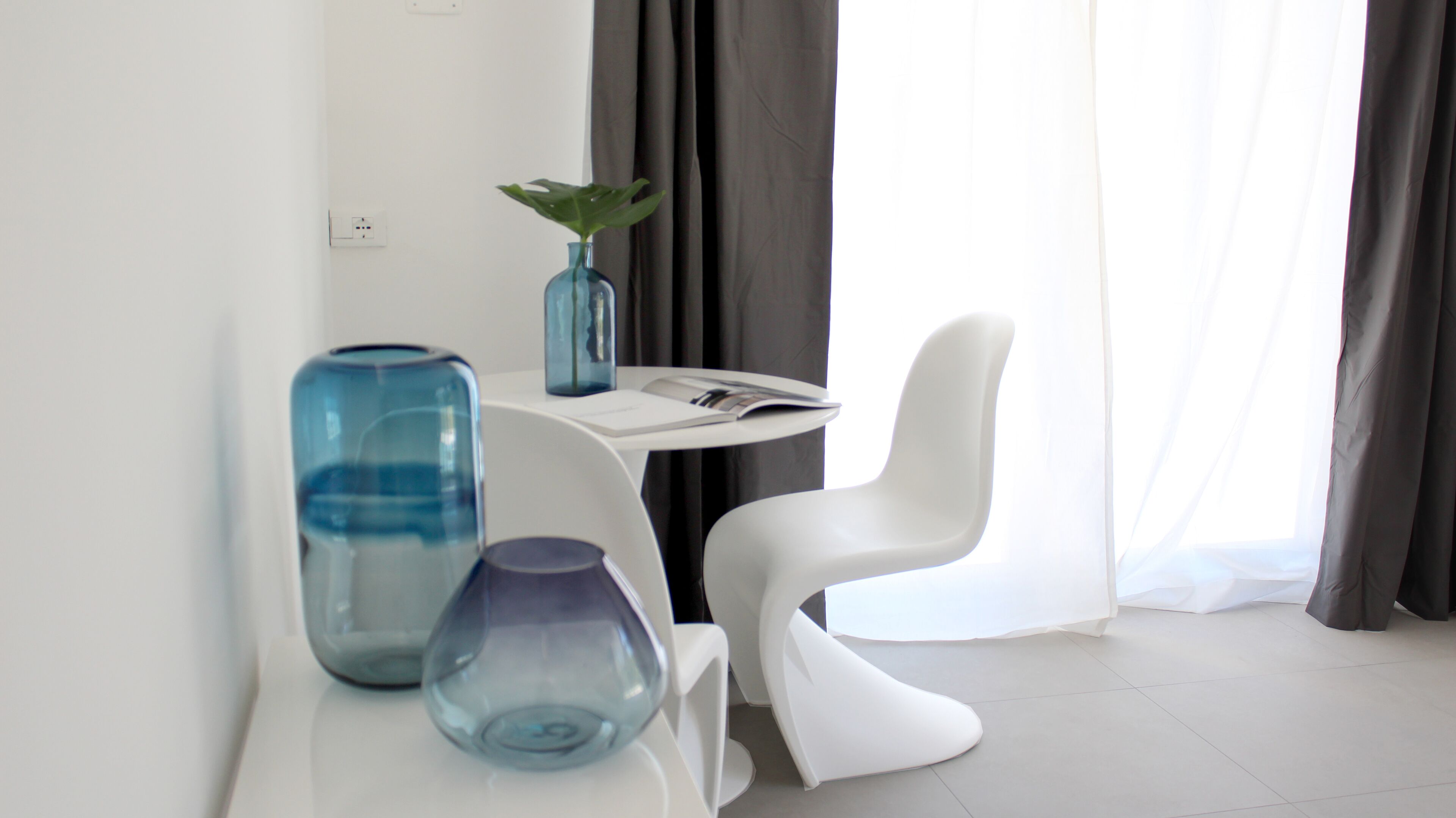 Una habitación moderna con una mesa blanca, dos jarrones azules, una silla blanca y una planta.