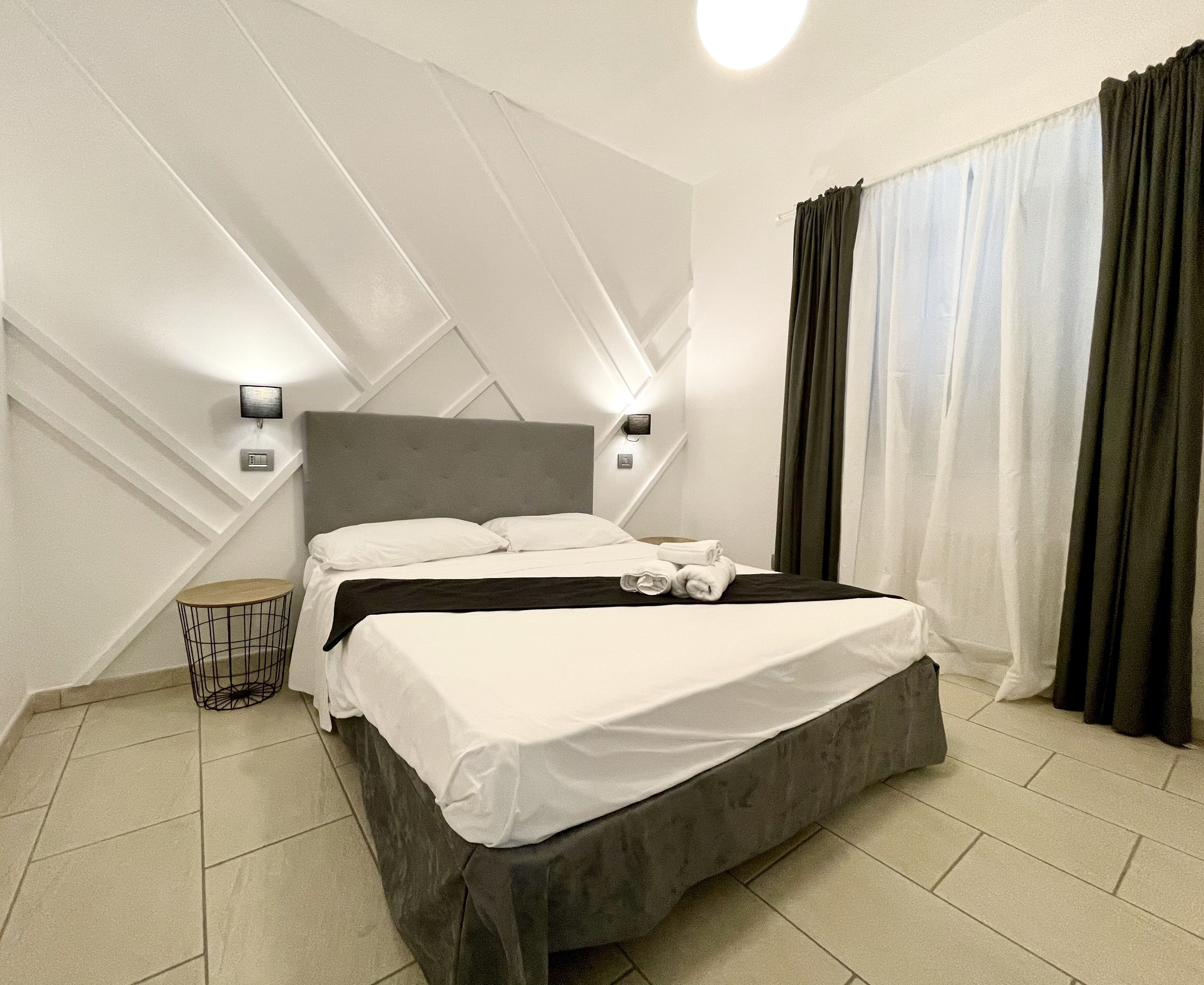 Ett modernt hotellrum med en stor säng, två sängbord, ett runt sidobord och en väggmonterad lampa.