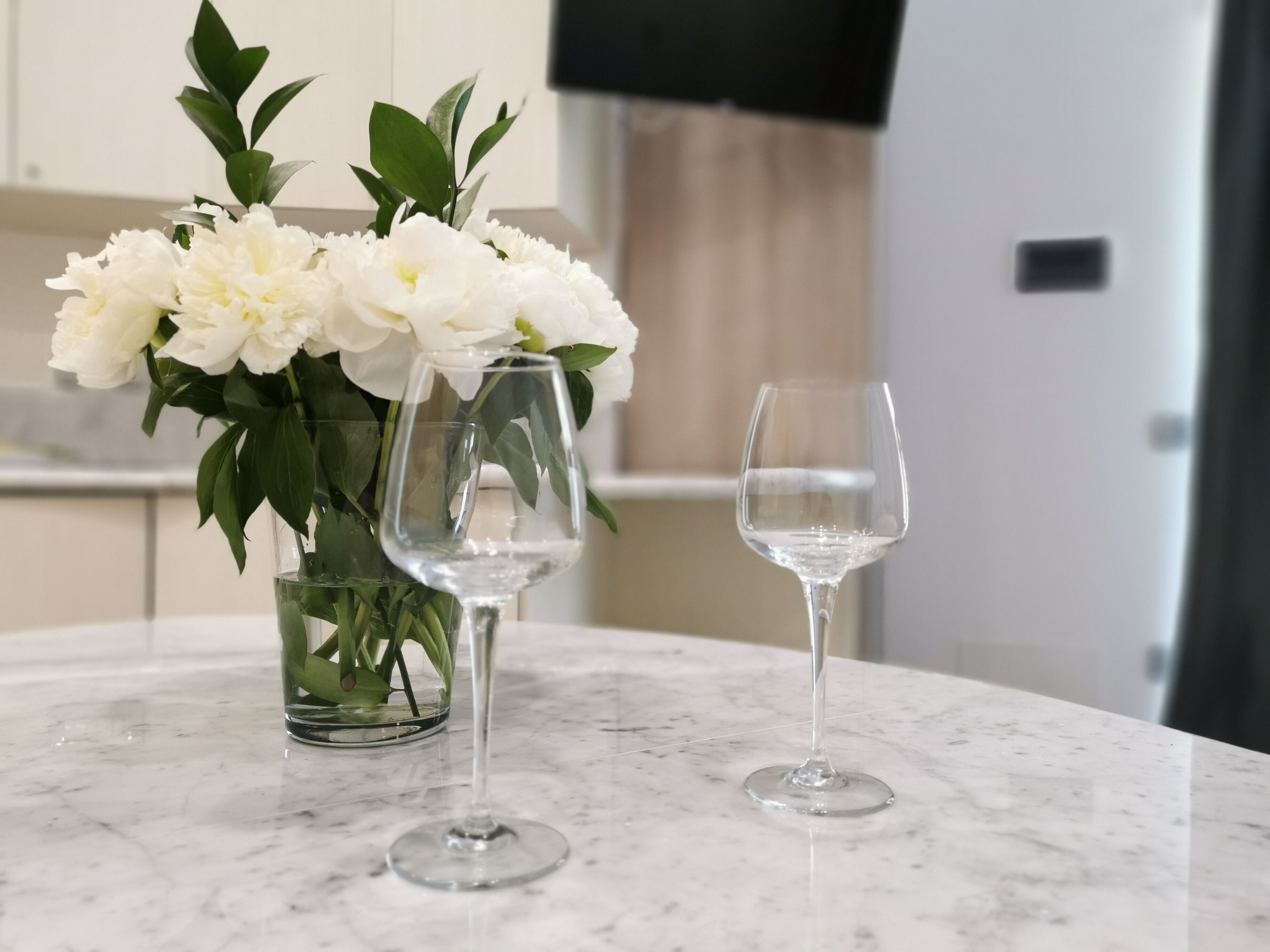 Una encimera de mármol con un jarrón de flores blancas y dos copas de vino.