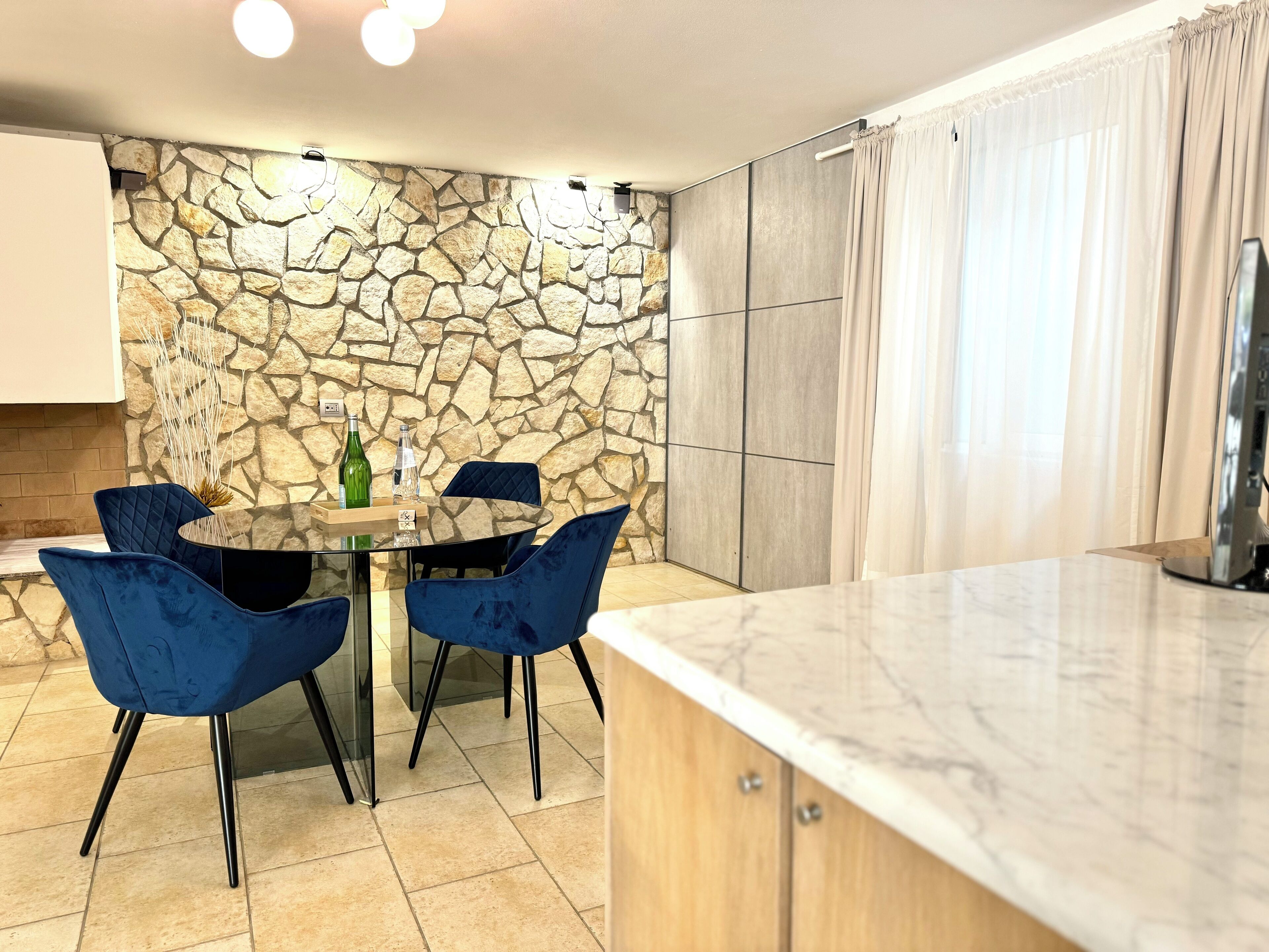 Una cocina moderna con pared de piedra, una mesa redonda de vidrio, sillas azules y encimera de mármol.