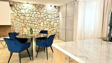 Una cocina moderna con pared de piedra, una mesa redonda de vidrio, sillas azules y encimera de mármol.