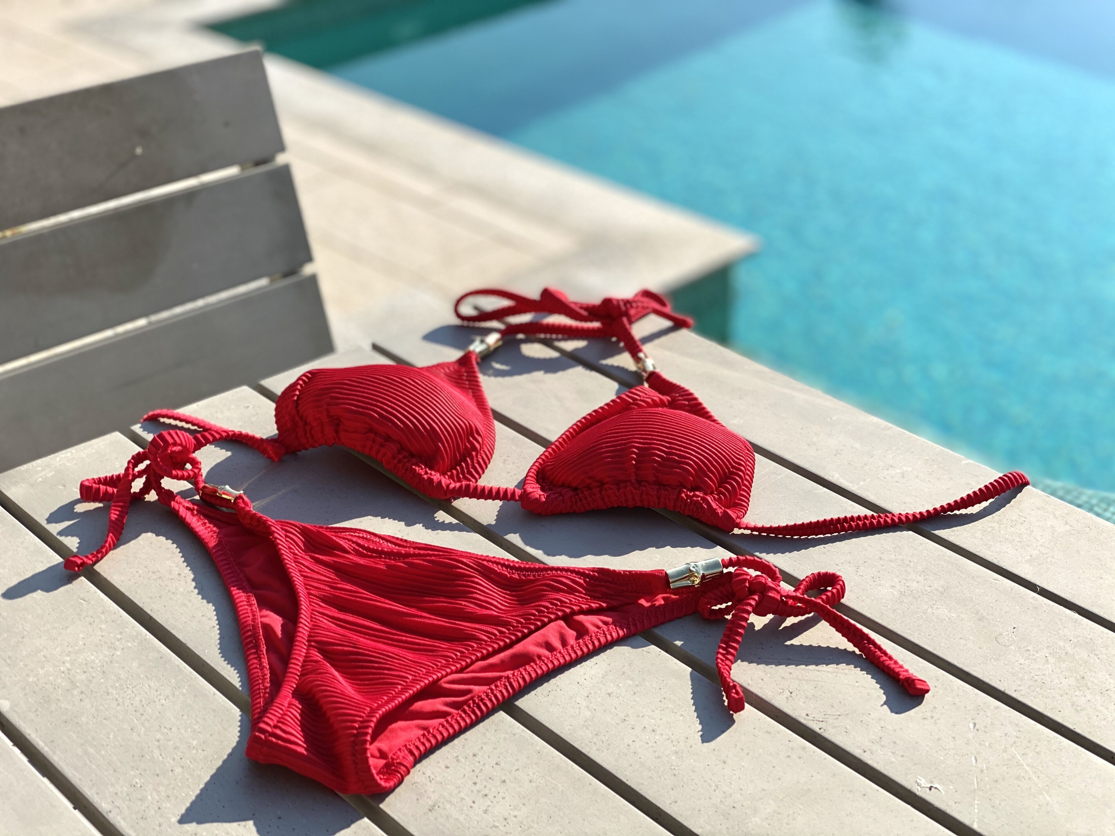 A pair of red bikinis on a white lounge chair by a pool.