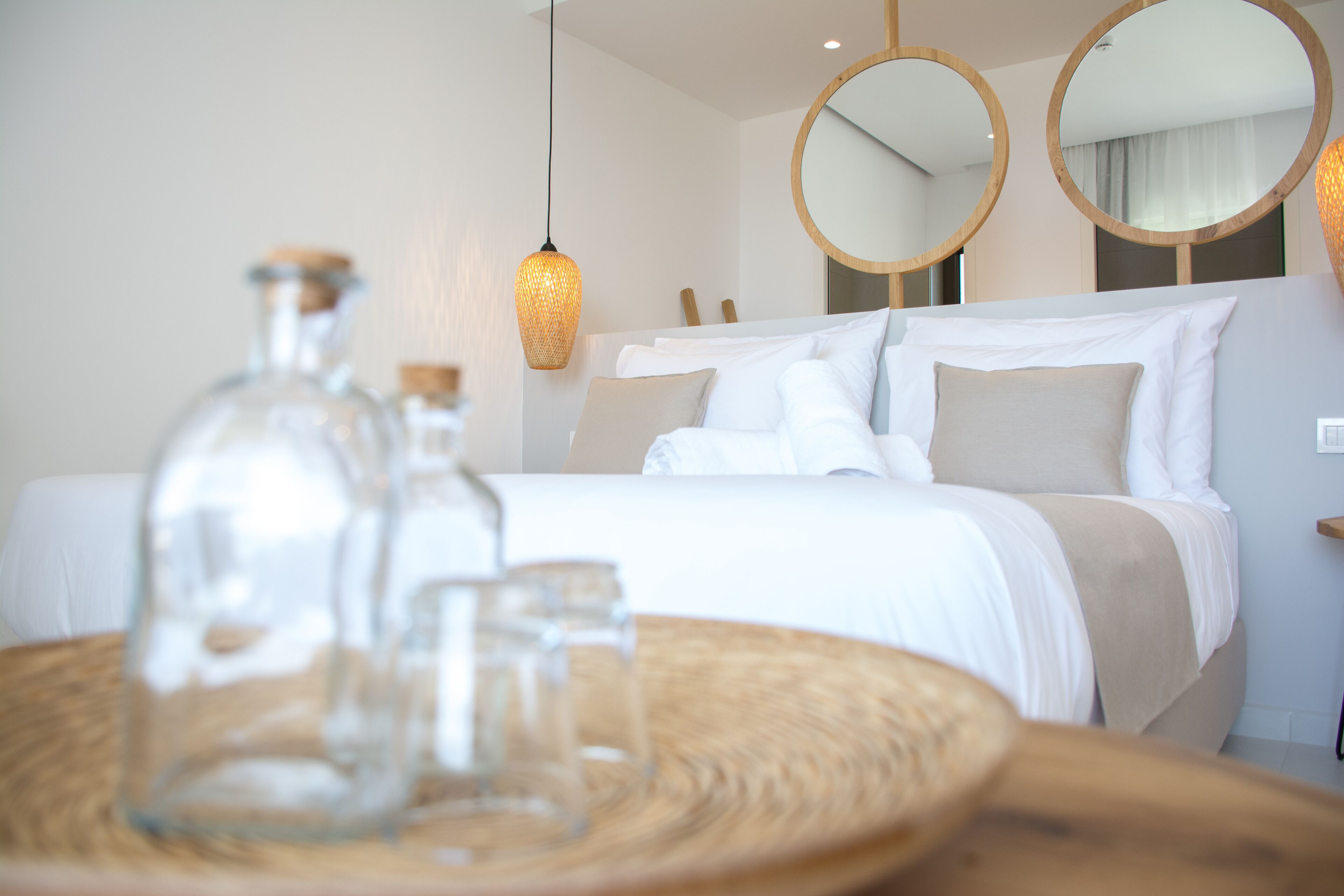 Een net opgemaakt bed met witte lakens, een ronde spiegel en een hanglamp in een moderne hotelkamer.