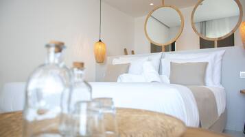 Een net opgemaakt bed met witte lakens, een ronde spiegel en een hanglamp in een moderne hotelkamer.